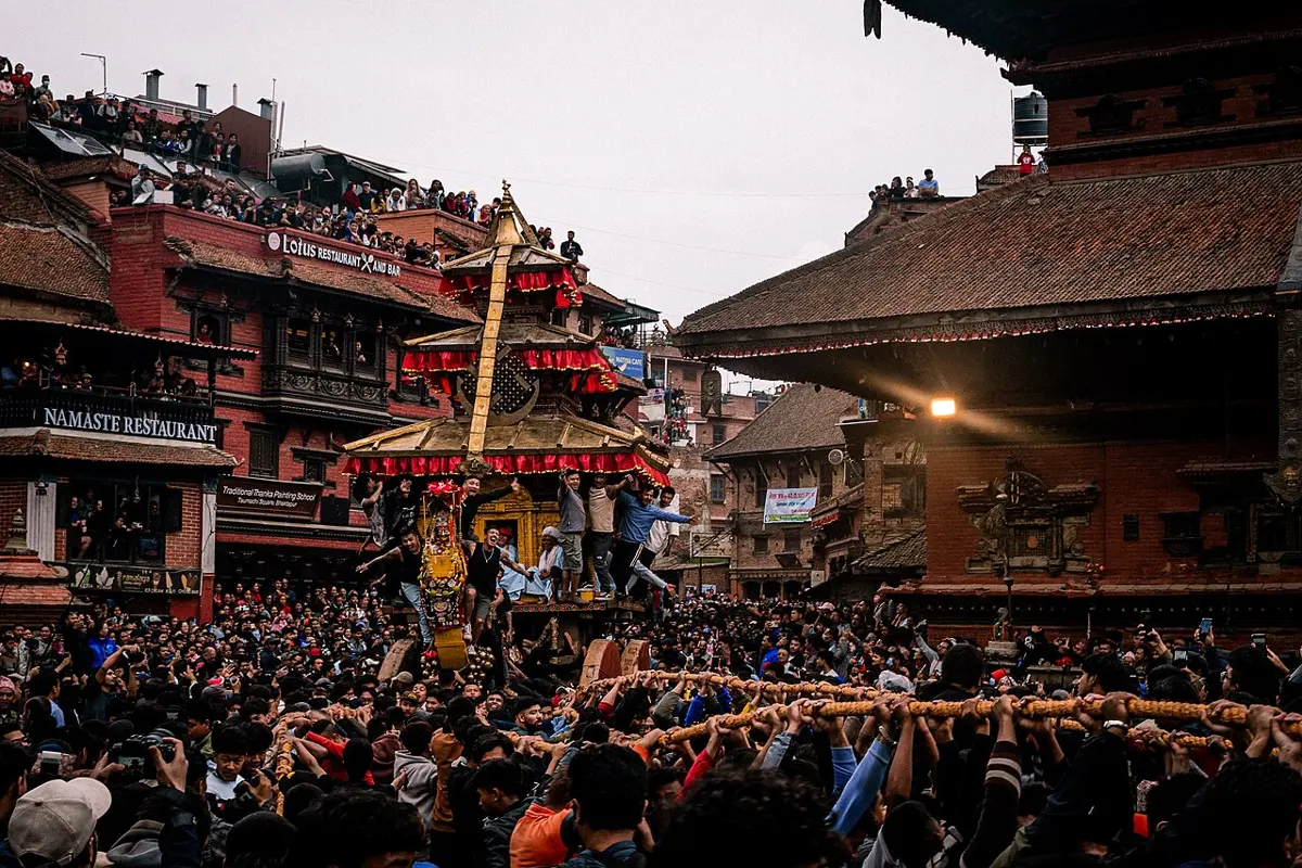 A tall golden chariot in a crowded square in Bhaktapur, with a thick rope held up by many hands in the foreground