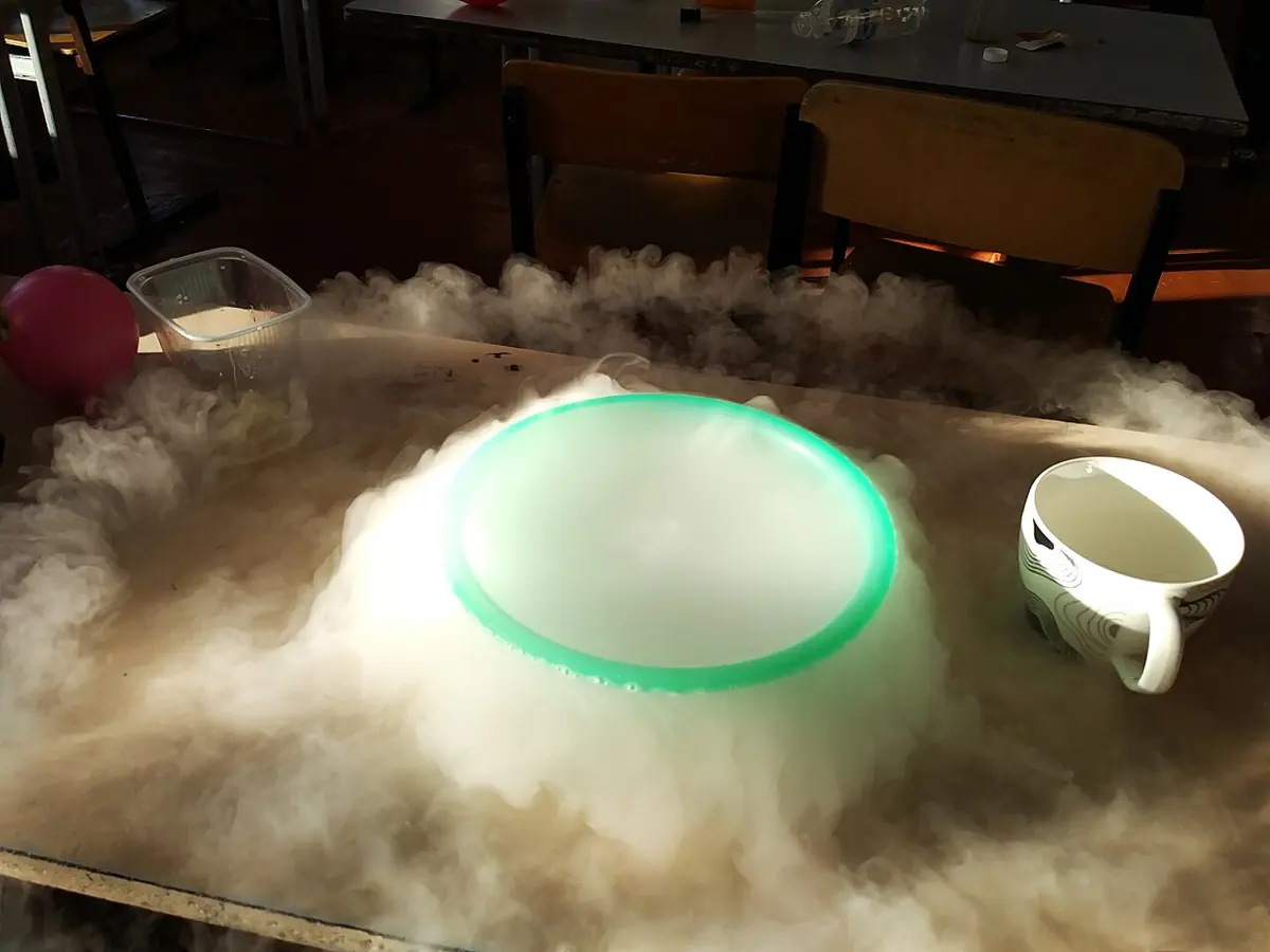 A bowl on a classroom table, overflowing with thick white fog that spreads across the table
