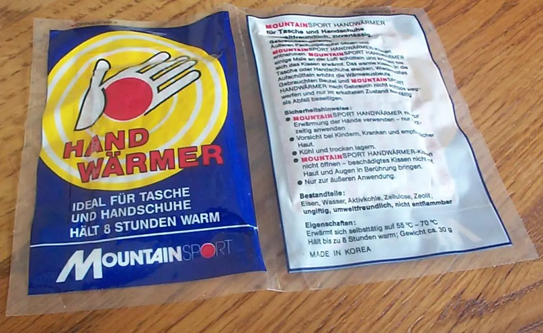 A disposable hand warmer in its printed plastic wrapper, front and back, lying on a wooden table