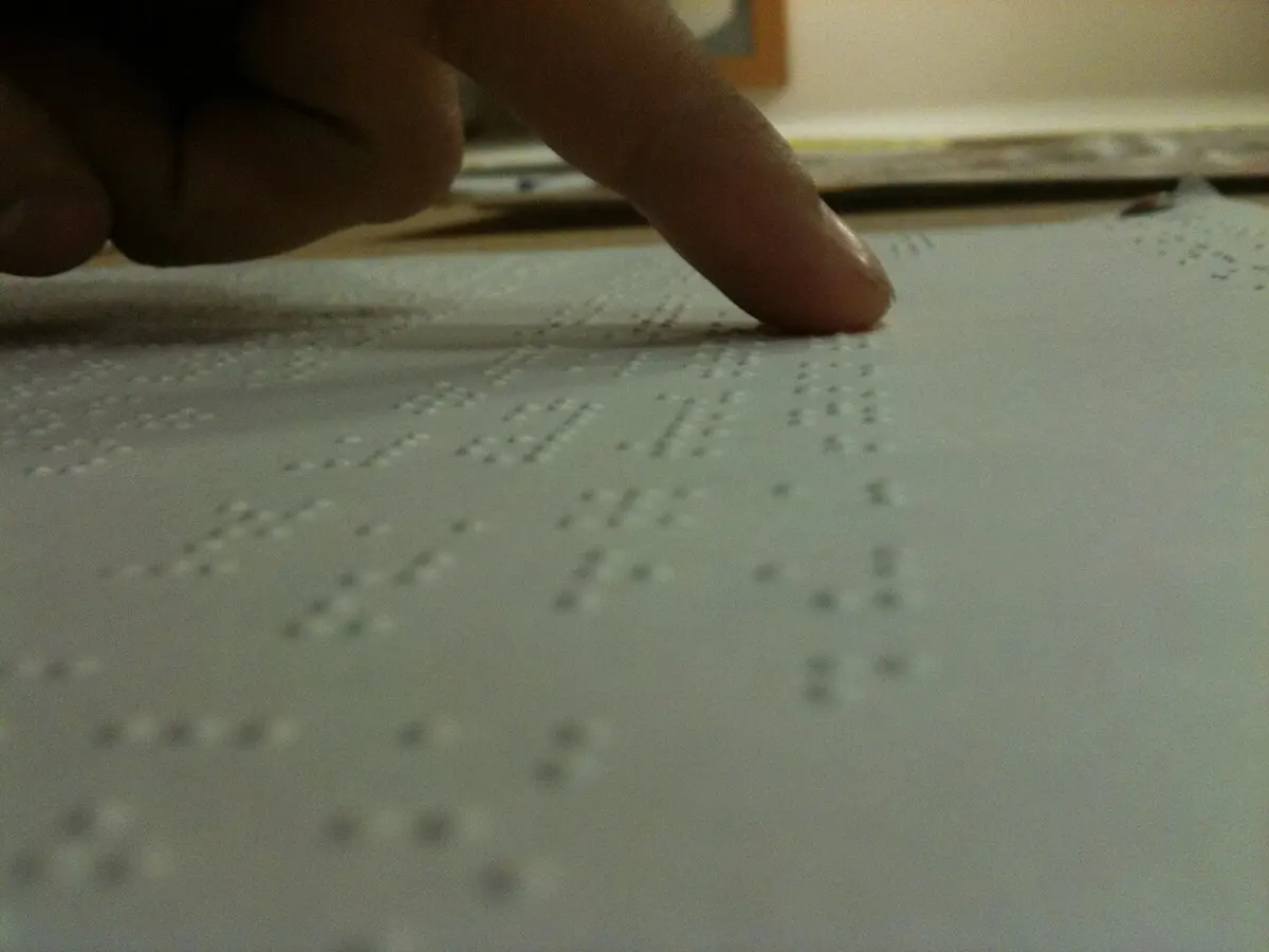 A fingertip resting on a page of raised Braille dots