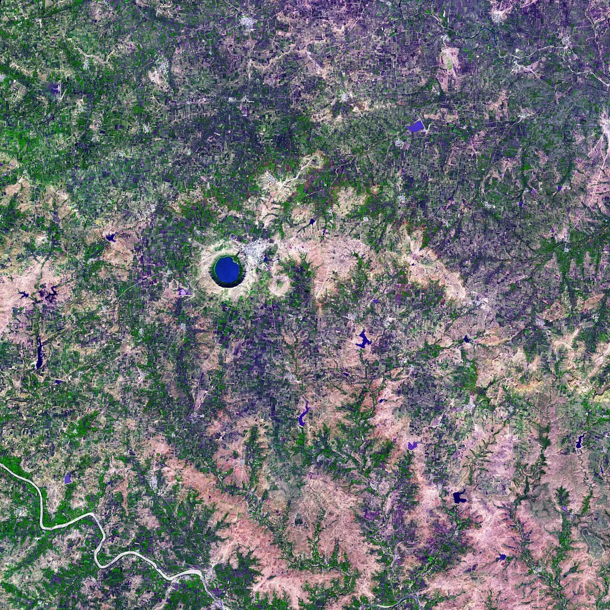 A satellite view of farmland in purple, green and pink, with a round dark lake in a pale ring near the center