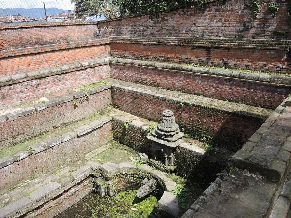 A sunken square courtyard of old red brick, with steps down on every side to a carved stone spout at the bottom, beside a small shrine