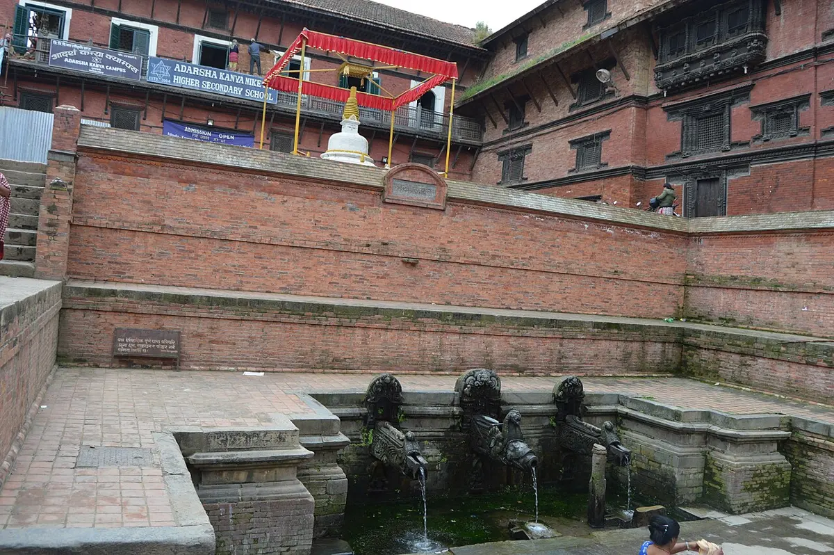 A sunken stone courtyard with brick walls, and three carved stone spouts at the far end with water running from them into a basin