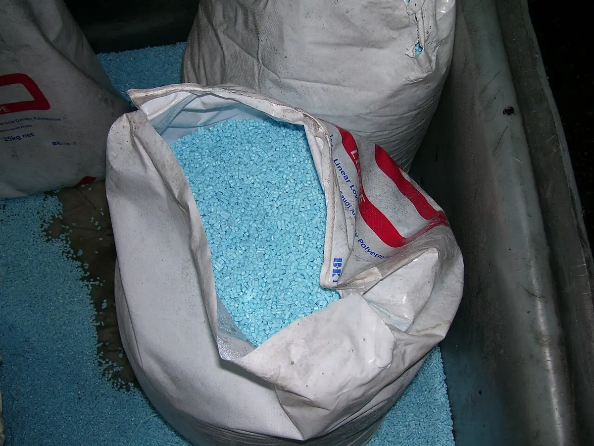 An open sack full of small pale blue plastic granules, with more granules spilled around it; the label on the sack says linear low density polyethylene
