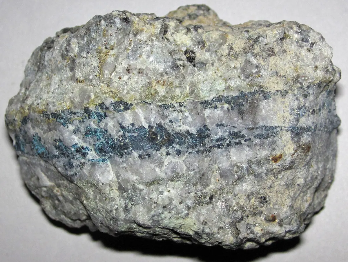 A palm-sized lump of pale gray rock crossed by a dark band of blue-gray and turquoise metal minerals