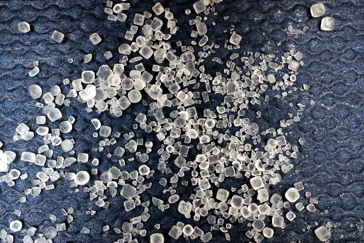 Hundreds of small, clear grains of table salt on a dark blue cloth, most of them little cubes