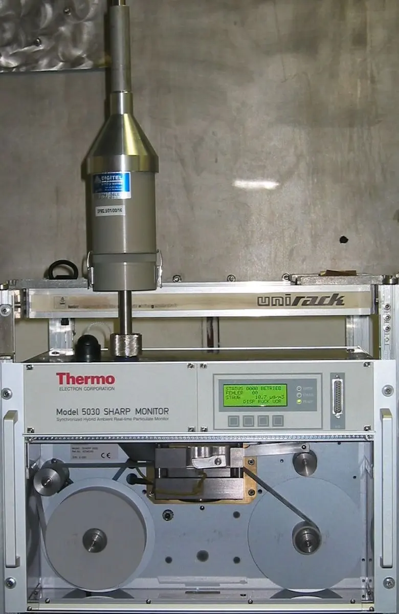 A gray metal instrument box with a display, a window showing two reels of filter tape, and a tall cylindrical metal inlet mounted on top