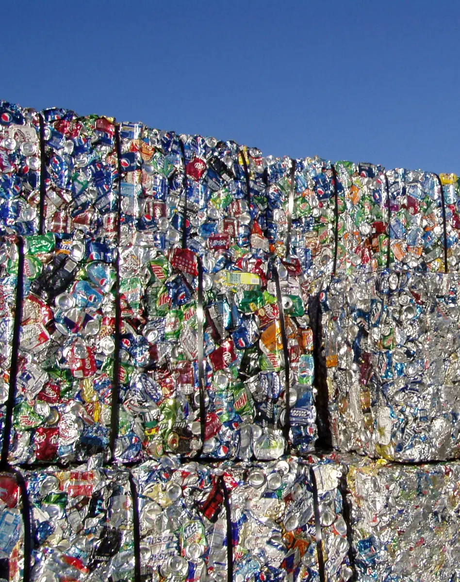 A stack of large blocks made of thousands of crushed aluminium cans in many colors, against a blue sky