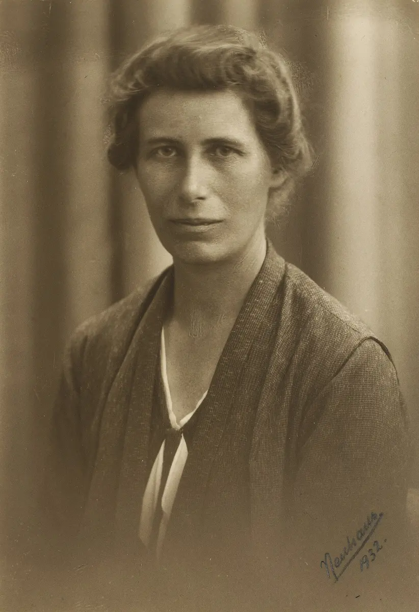 A black-and-white photograph of a young woman with short hair, in a dark dress, looking at the camera
