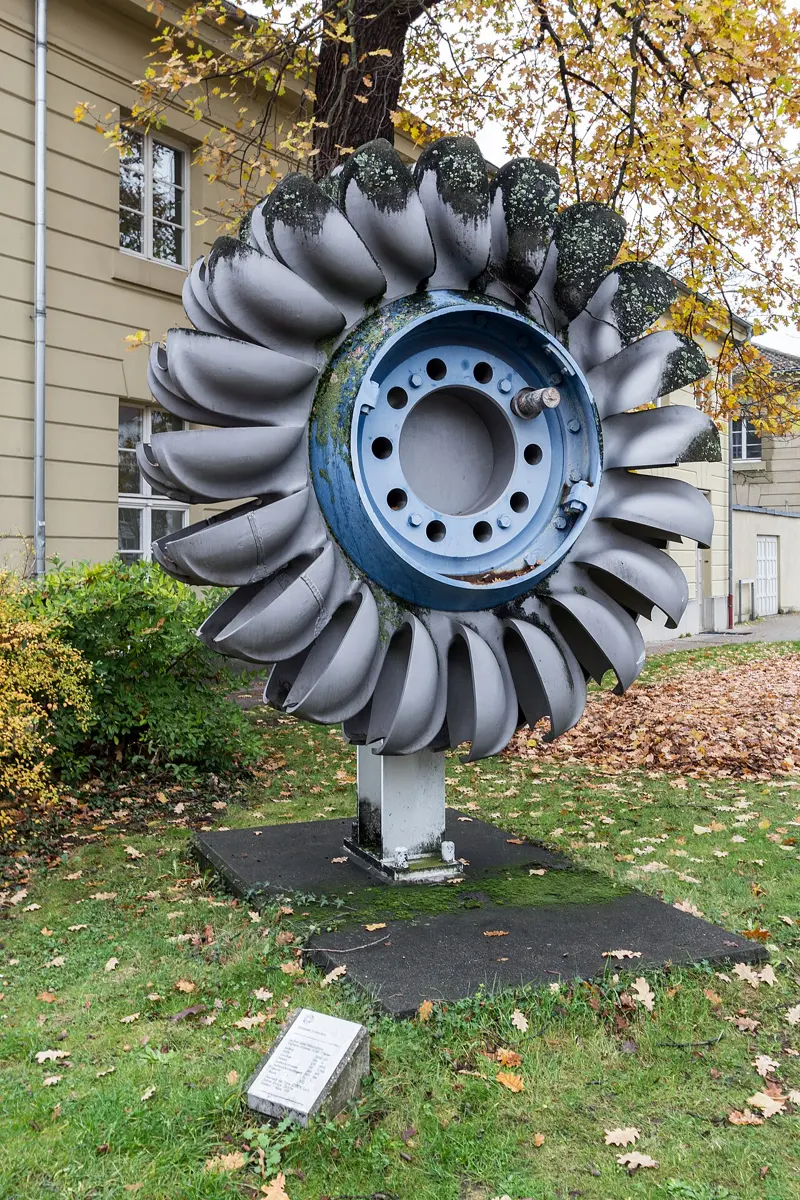 A large metal wheel standing on its edge, with rows of curved double cups all round its rim