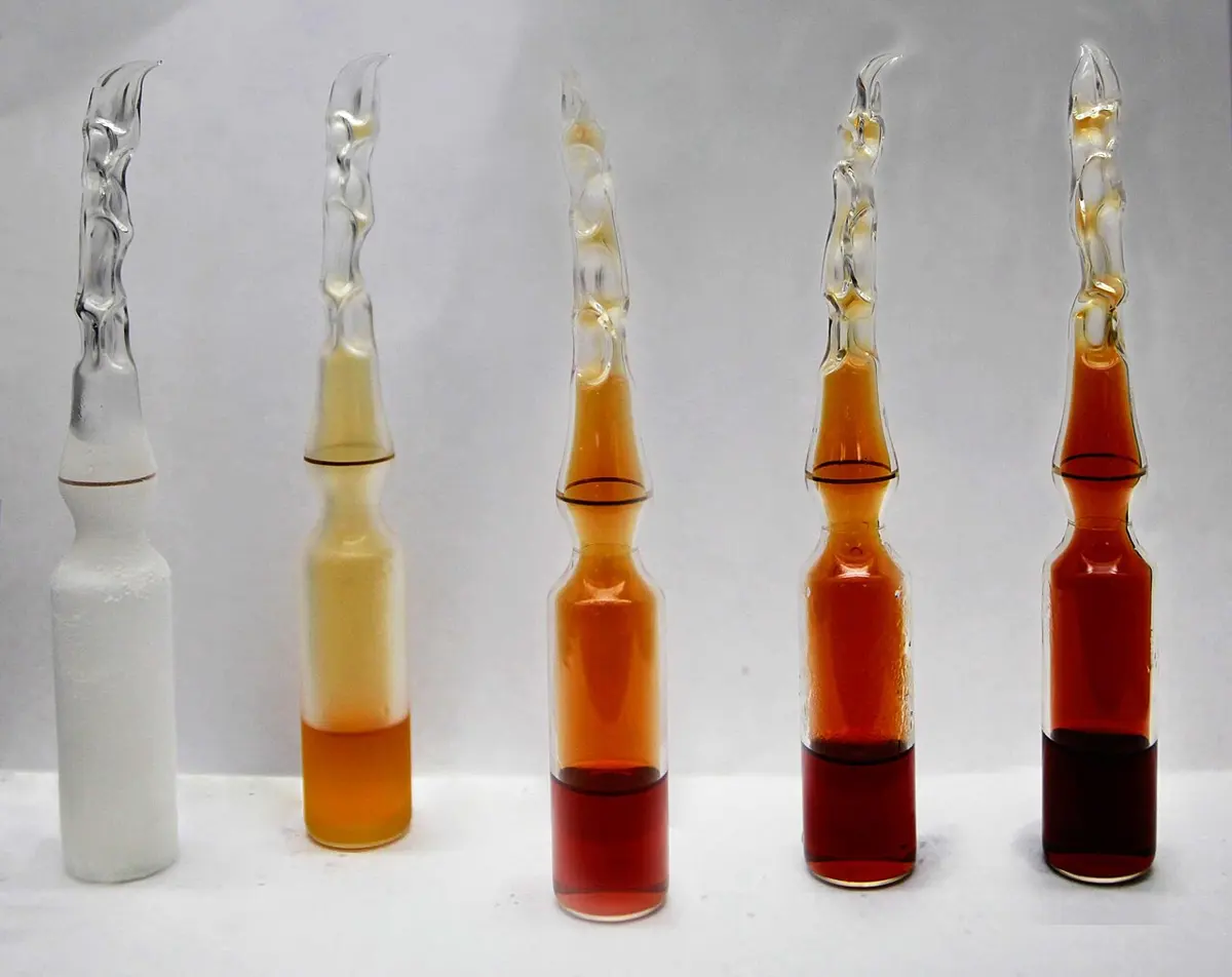 The same sealed glass ampoule shown five times in a row. The first is frosted white; the next holds a pale yellow gas over a yellow liquid; the last three hold gas that is orange, then deeper red-brown, then darkest, over dark red liquid