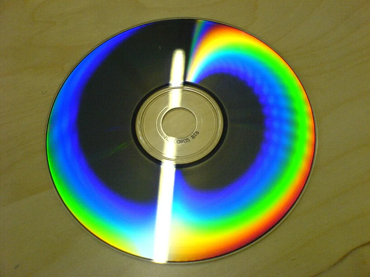 A CD lying on a table, its surface showing bright bands of rainbow colors