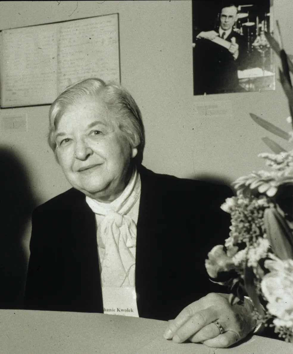 A black-and-white photograph of Stephanie Kwolek, an older woman with short gray hair, smiling, seated at a table