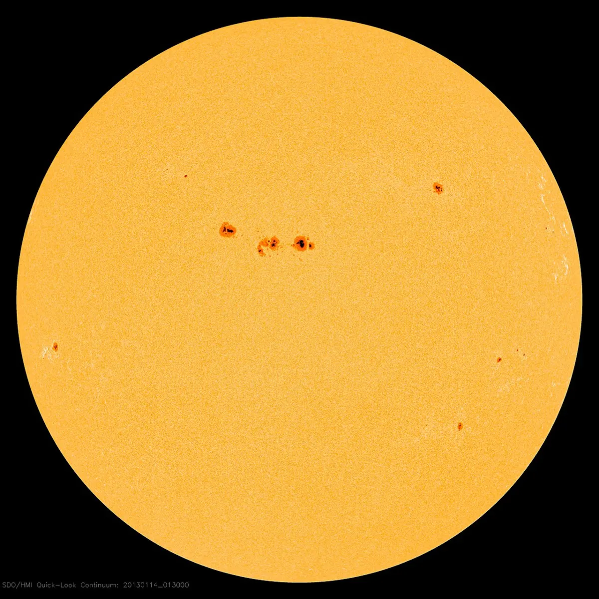 The disc of the Sun, yellow-orange, with a row of dark spots near the middle and a few smaller ones scattered elsewhere