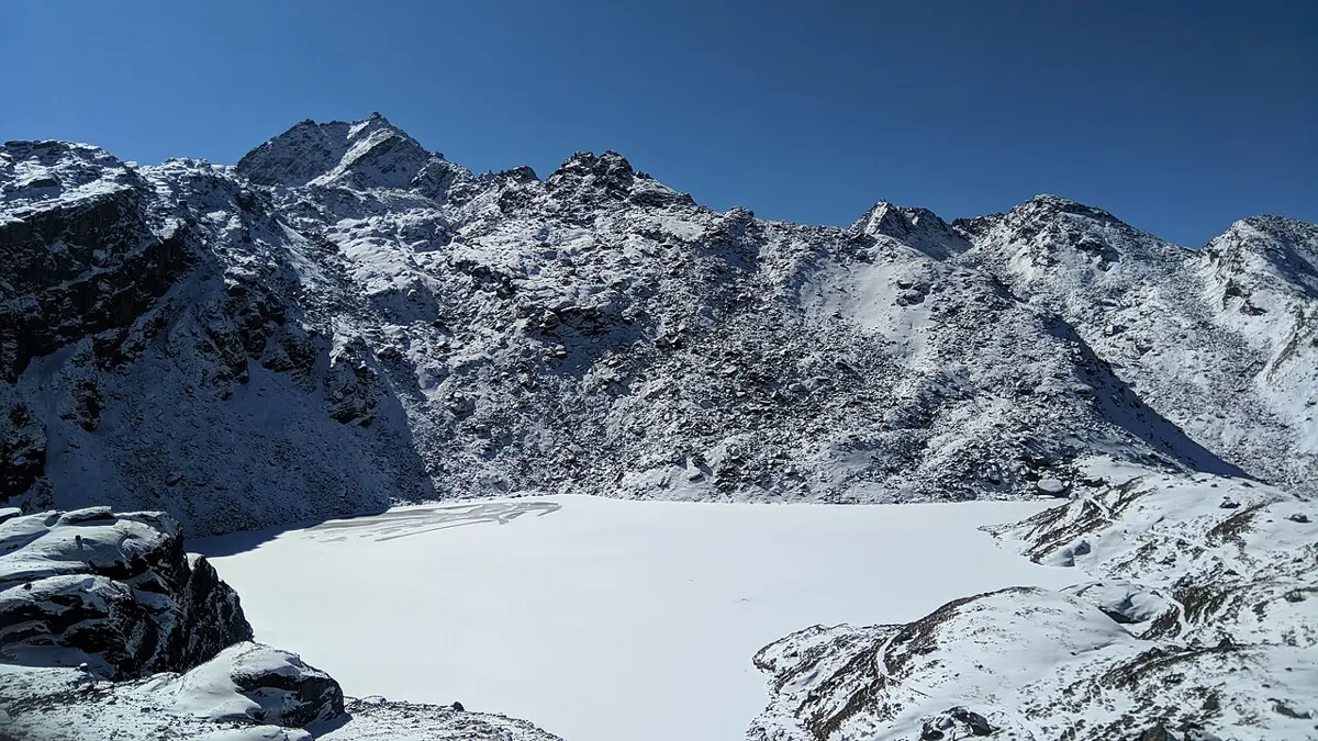 चट्टानी र हिउँले ढाकिएका पहाडले घेरिएको, सेतो बरफ र हिउँले ढाकिएको ताल; माथि निलो आकाश