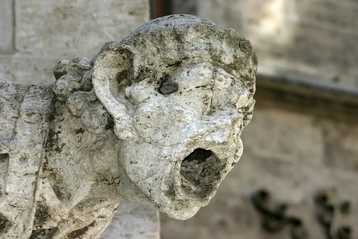 A stone gargoyle on an old building, its face worn rough and its features blurred