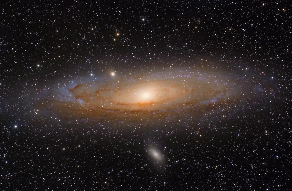 A large oval spiral galaxy, bright yellowish in the center with dark dust lanes, tilted almost edge-on, with two smaller fuzzy galaxies beside it