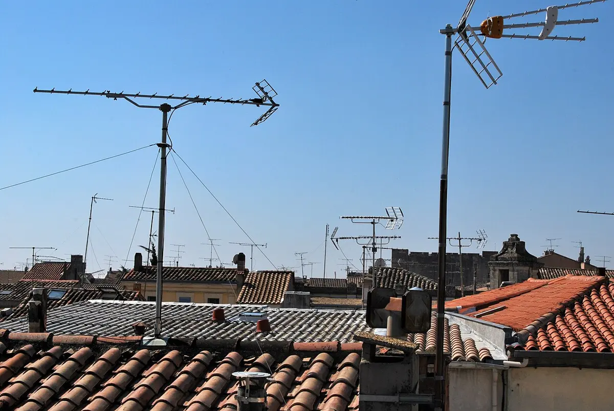 TV antennas on poles above red tiled roofs: each is a long metal rod with many short crossbars, pointing the same way