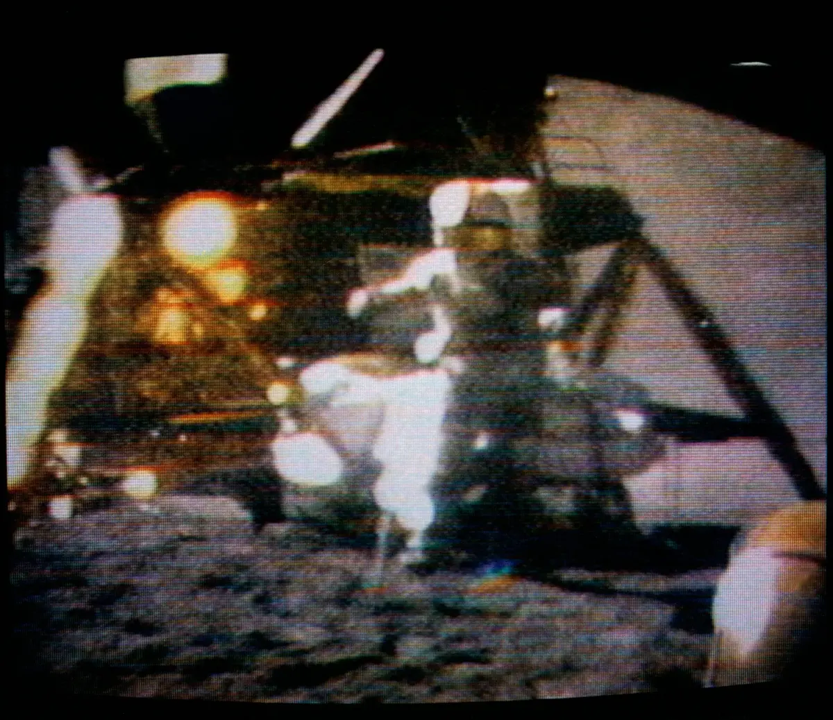 A blurry television picture of an astronaut in a white spacesuit standing on the gray surface of the Moon