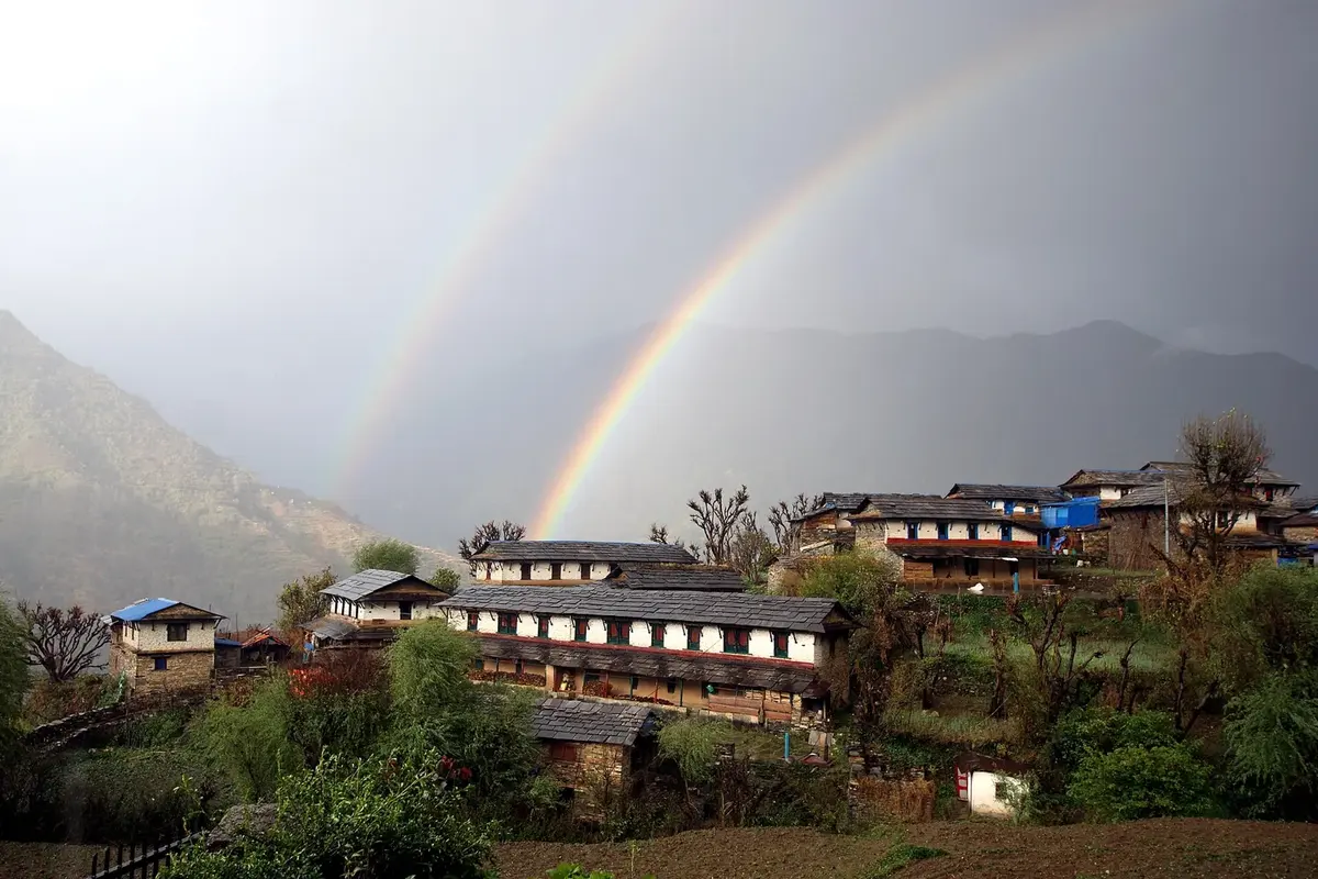 A double rainbow arching over green terraced hills and village houses at Ghandruk