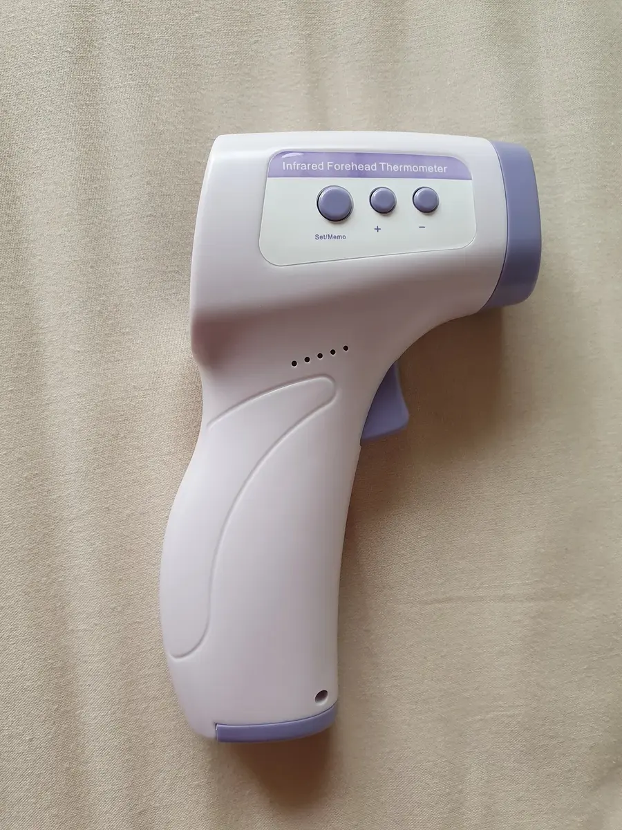 A white plastic infrared thermometer shaped like a small gun, with a display and buttons