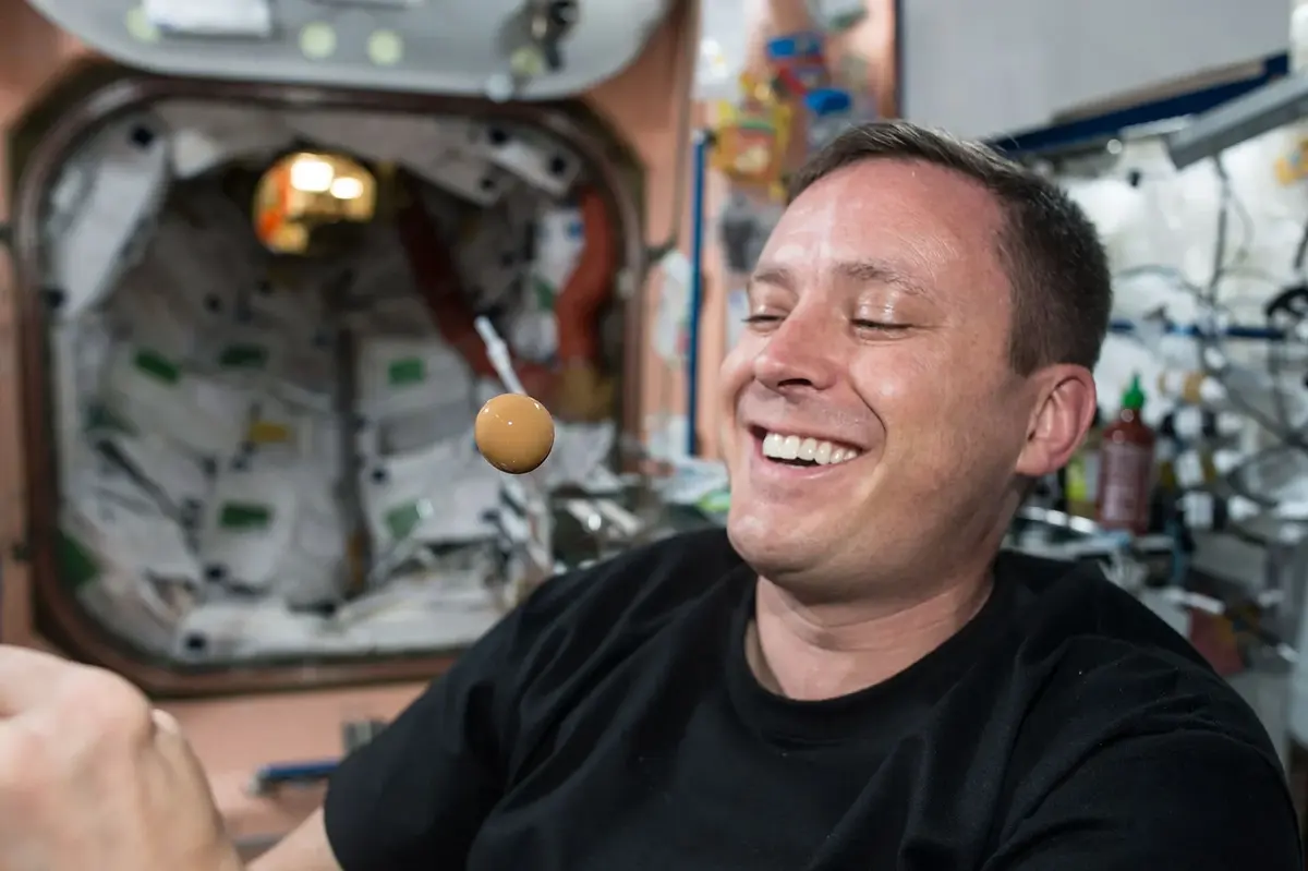 An astronaut in the Space Station watching a ball of liquid floating in the air in front of his face