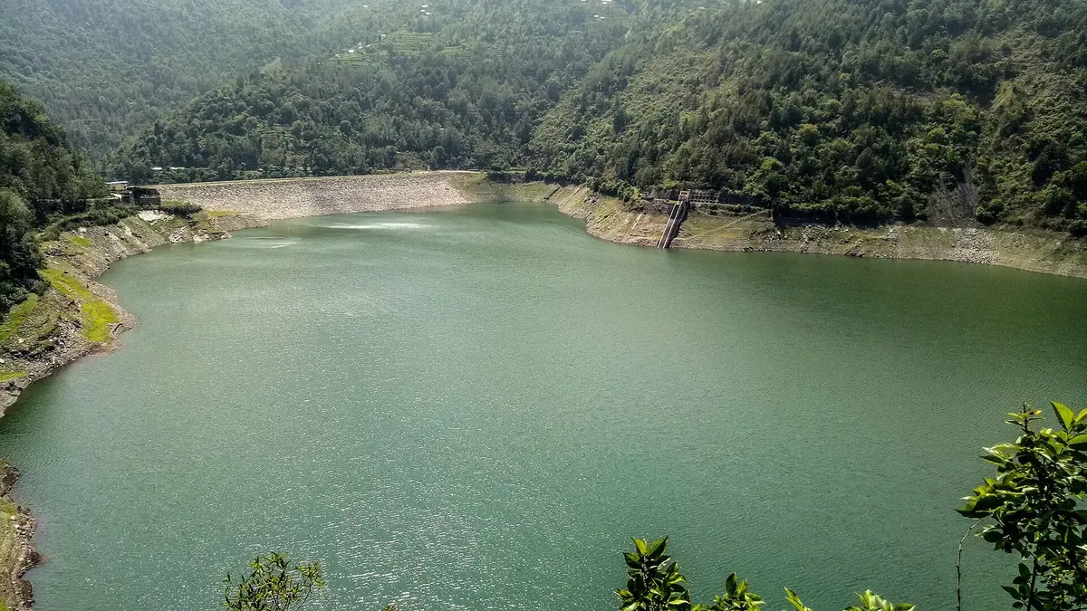 A green reservoir lake between forested hills, with the dam wall at its far end