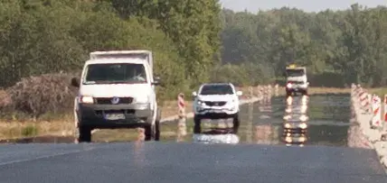 A long straight road with what looks like shining water across it in the distance, reflecting cars