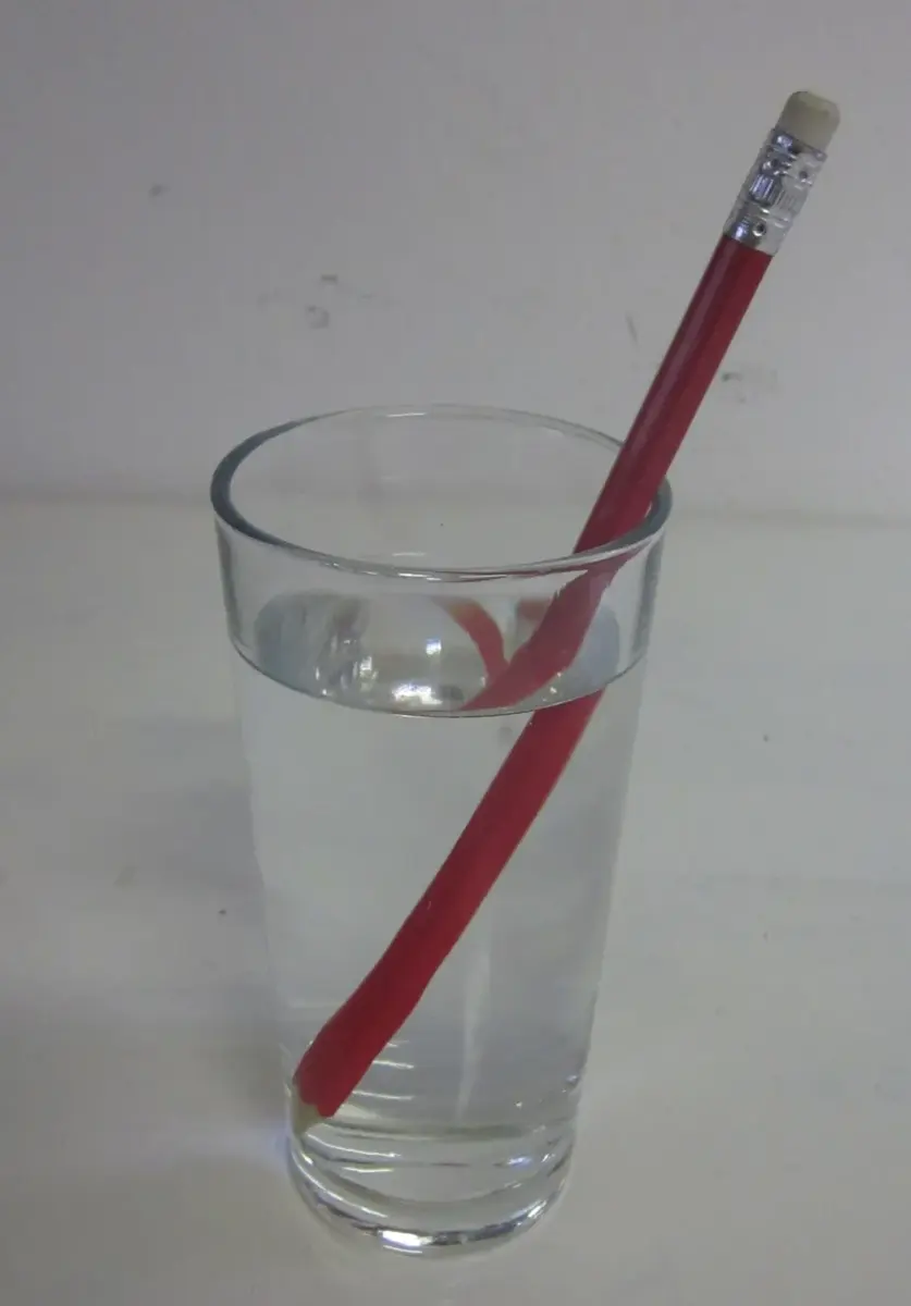 A pencil standing slanted in a glass of water, looking broken where it enters the water