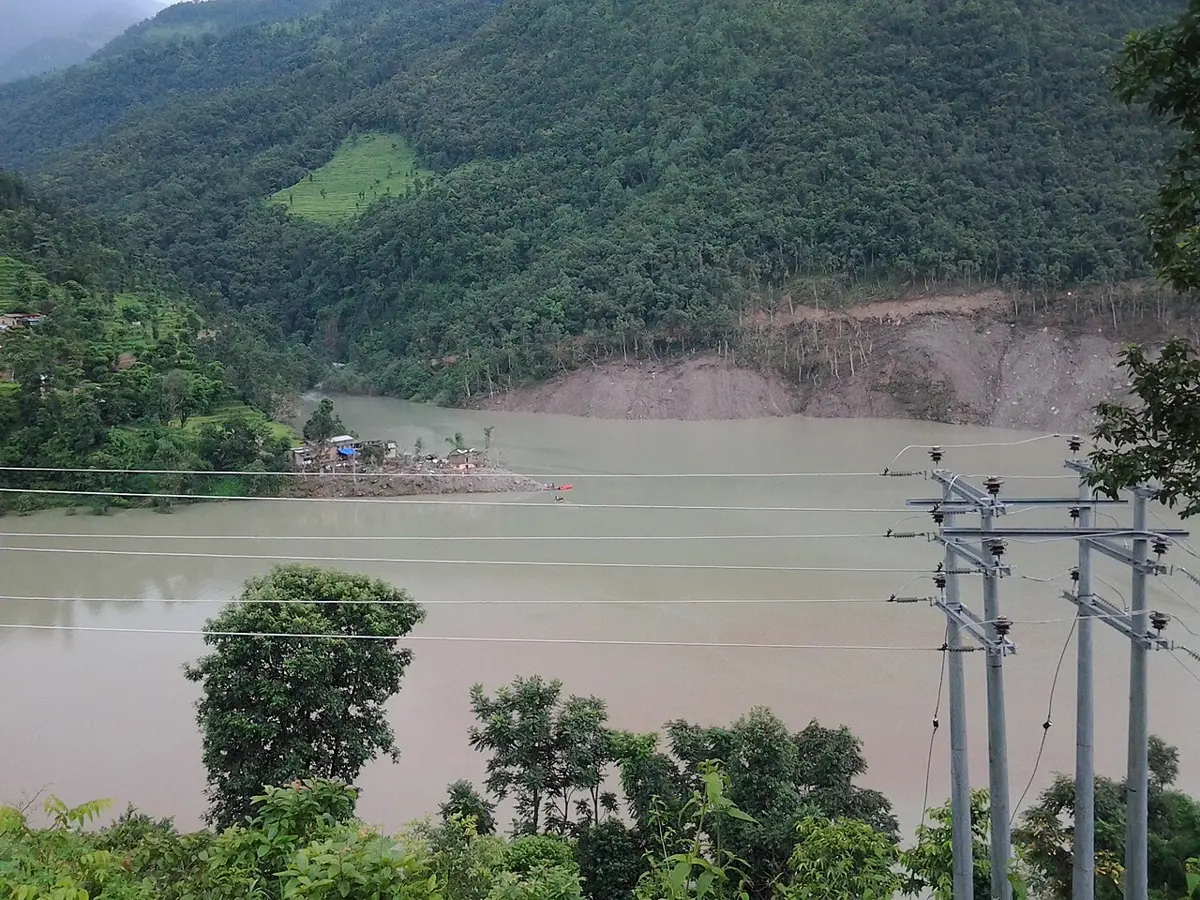 हरियो उपत्यका भरिने गरी फैलिएको धमिलो ताल, पारिको डाँडामा पहिरो गएर नाङ्गो देखिएको भाग