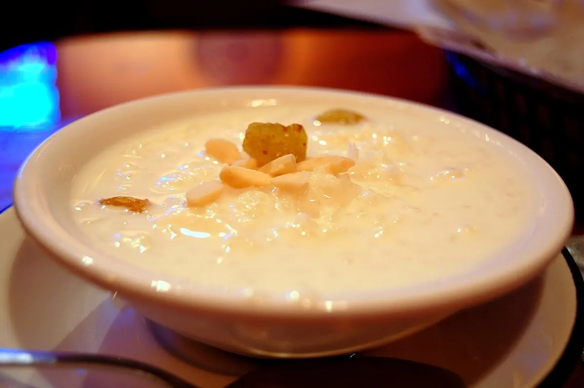 A bowl of creamy white rice pudding topped with sliced almonds and raisins
