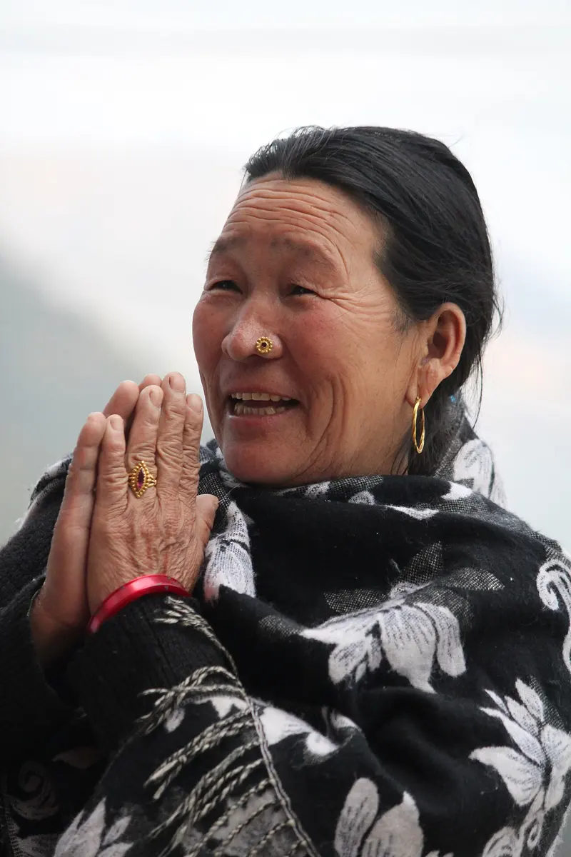 A smiling woman in a shawl joins her palms together in greeting