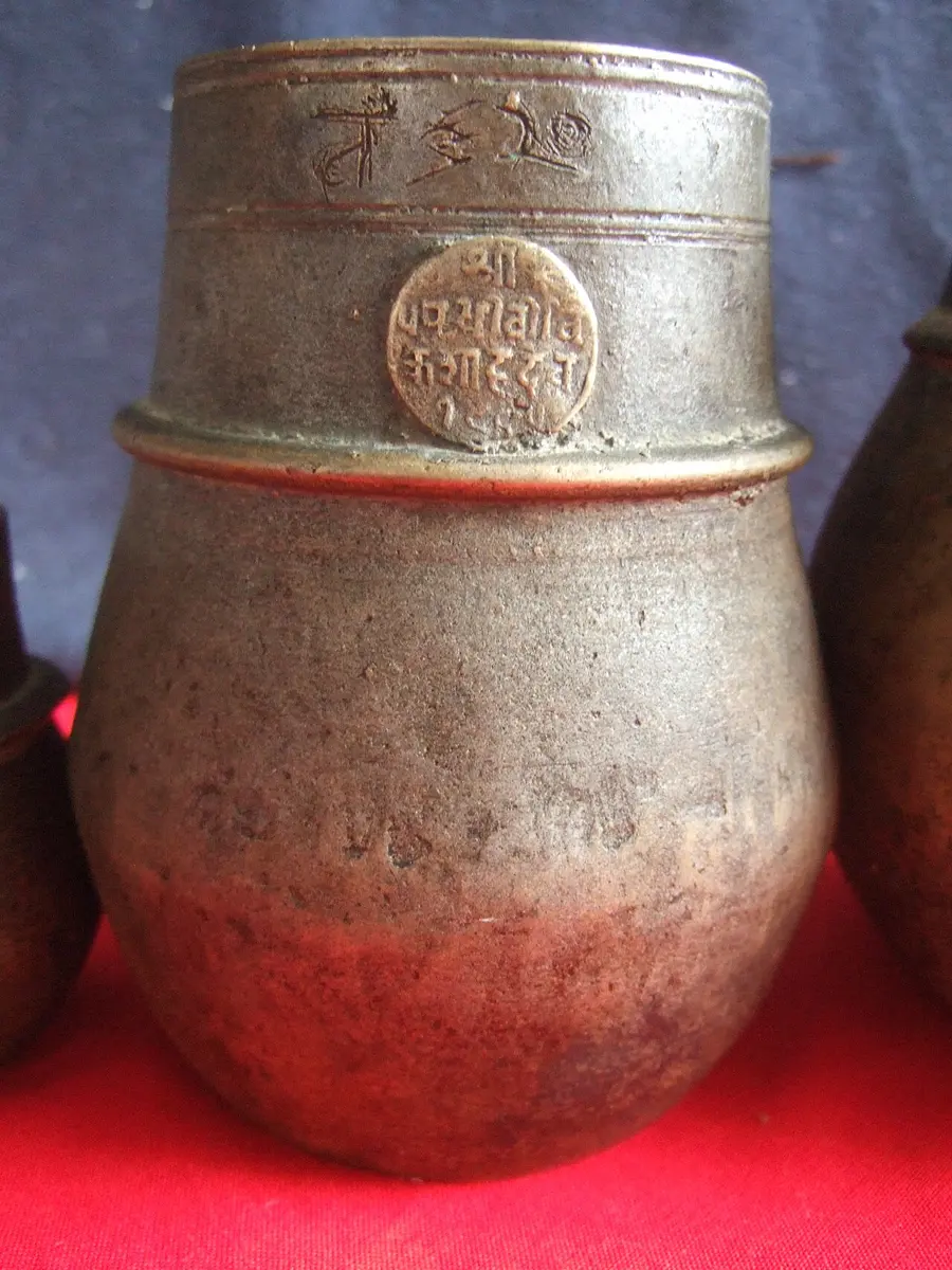 An old brass pot with a narrow neck and a round seal stamped on it, used in Nepal to measure grain
