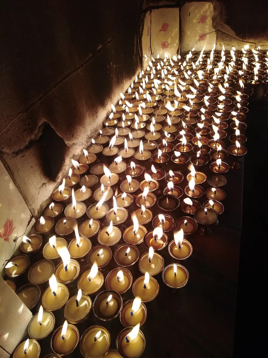 Rows of small lit lamps in metal cups, burning on a ledge
