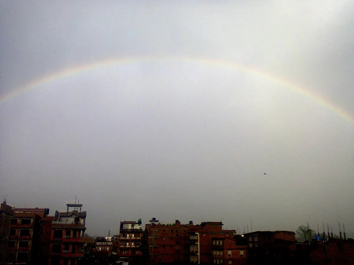 A rainbow arching over the roofs of houses in Bhaktapur under a gray sky