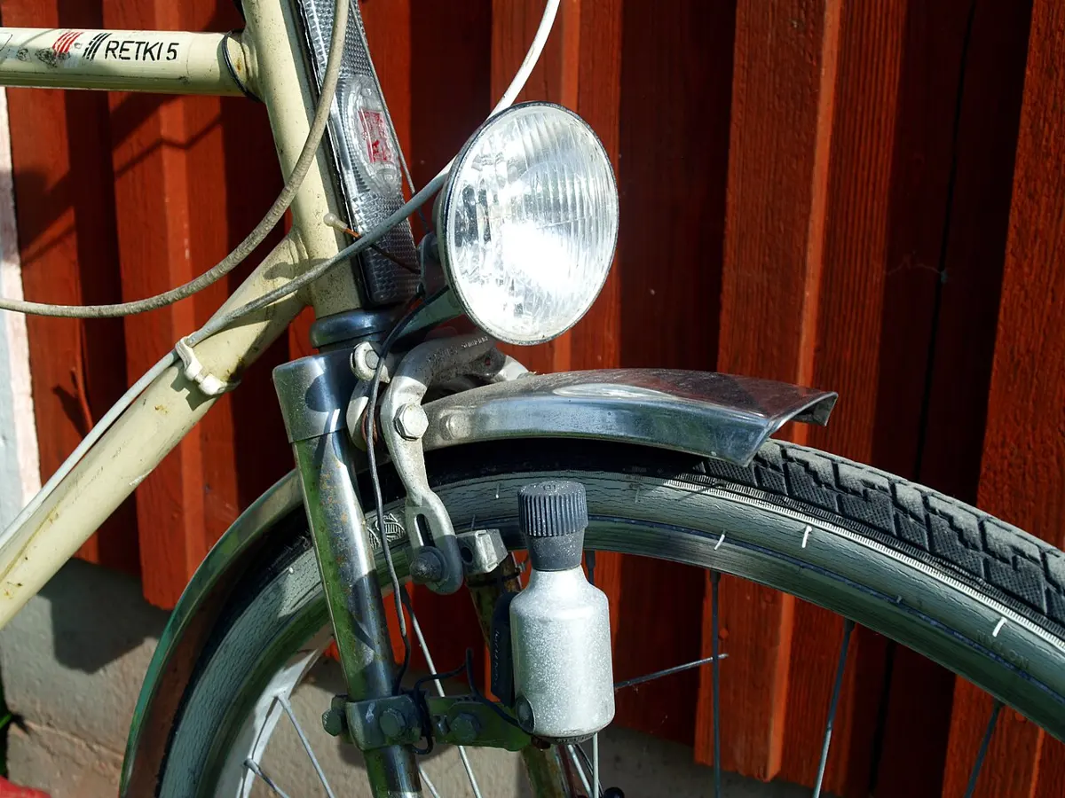 A small bottle-shaped dynamo fixed beside a bicycle's tyre, with a wire to the front lamp