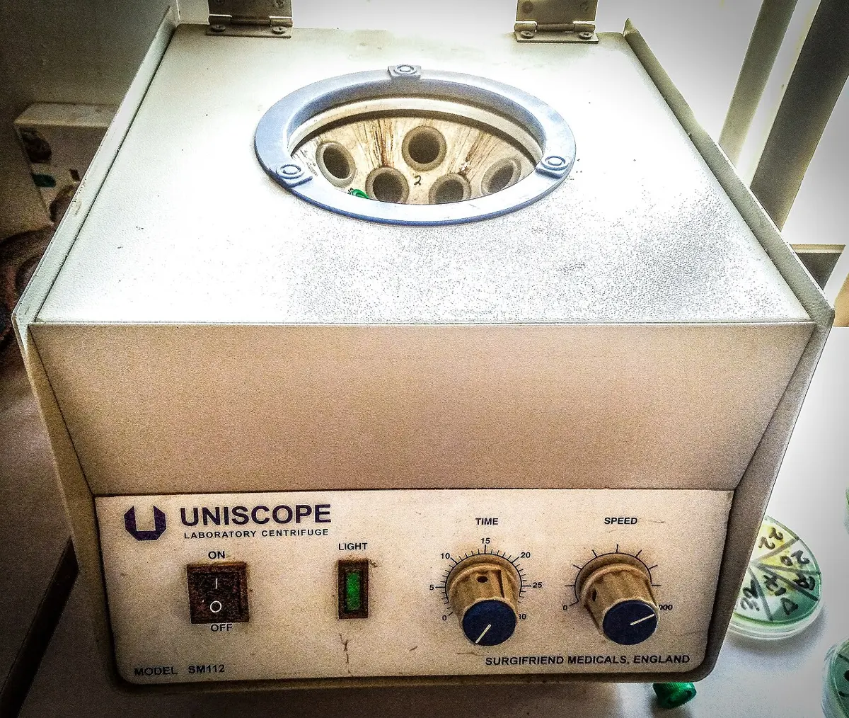 A laboratory centrifuge with its lid open, showing the holders for test tubes inside