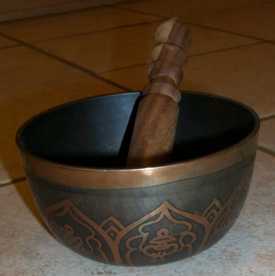 A dark metal singing bowl with a wooden striker resting in it.