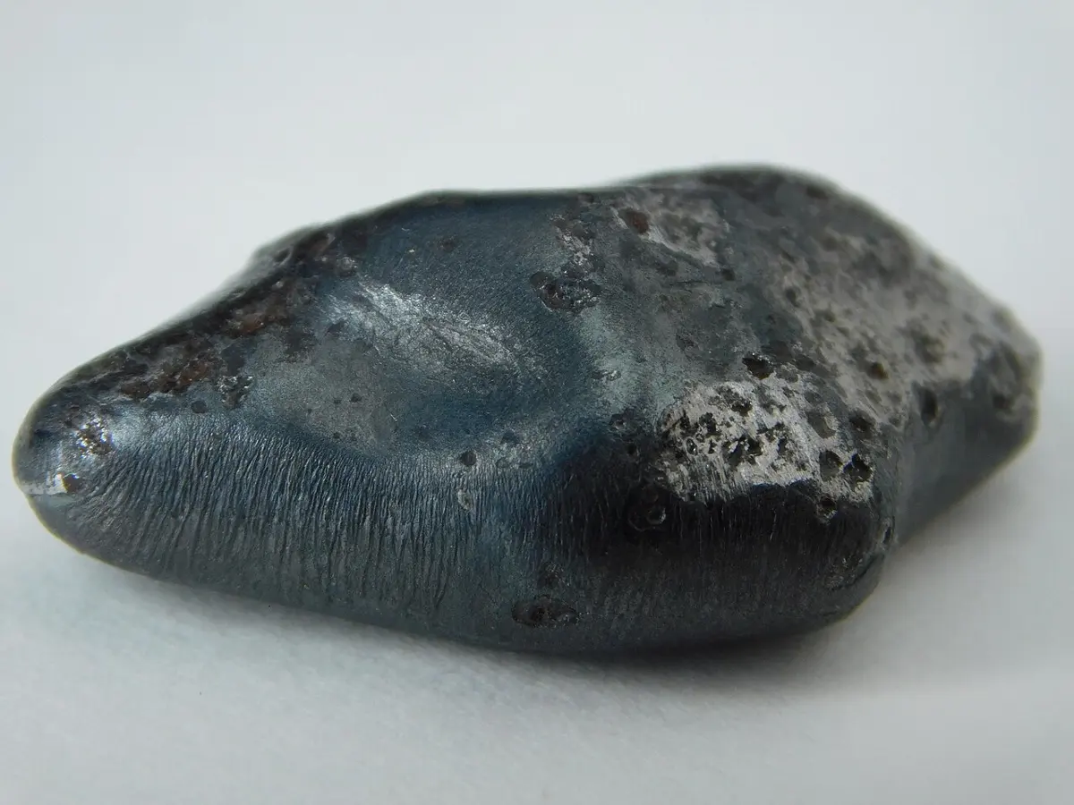 A smooth, dark gray, rounded lump of metal with small dents on its surface, on a white background