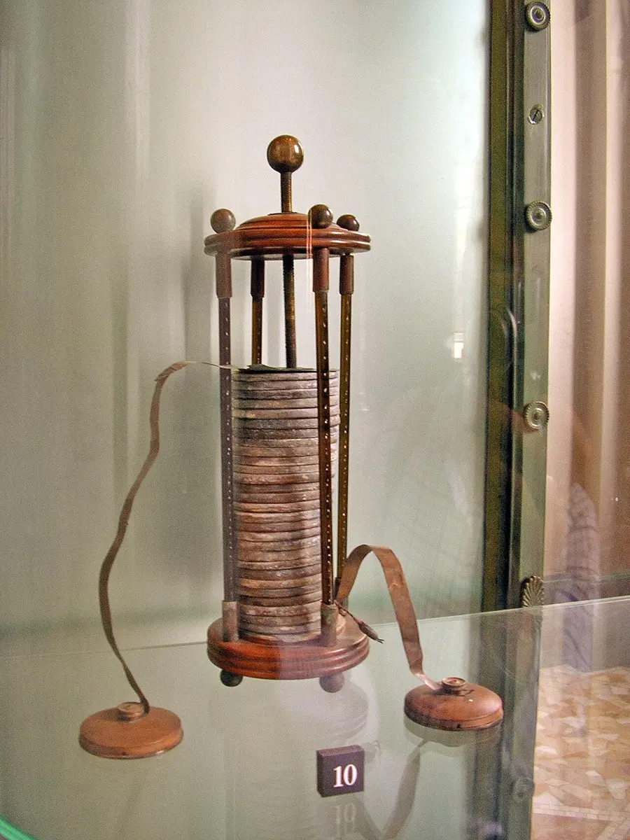 A tall stack of round metal discs held between four rods on a wooden base, in a glass museum case
