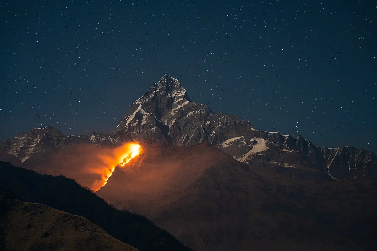 At night, a line of orange fire burns along a dark forested ridge below a snowy mountain peak