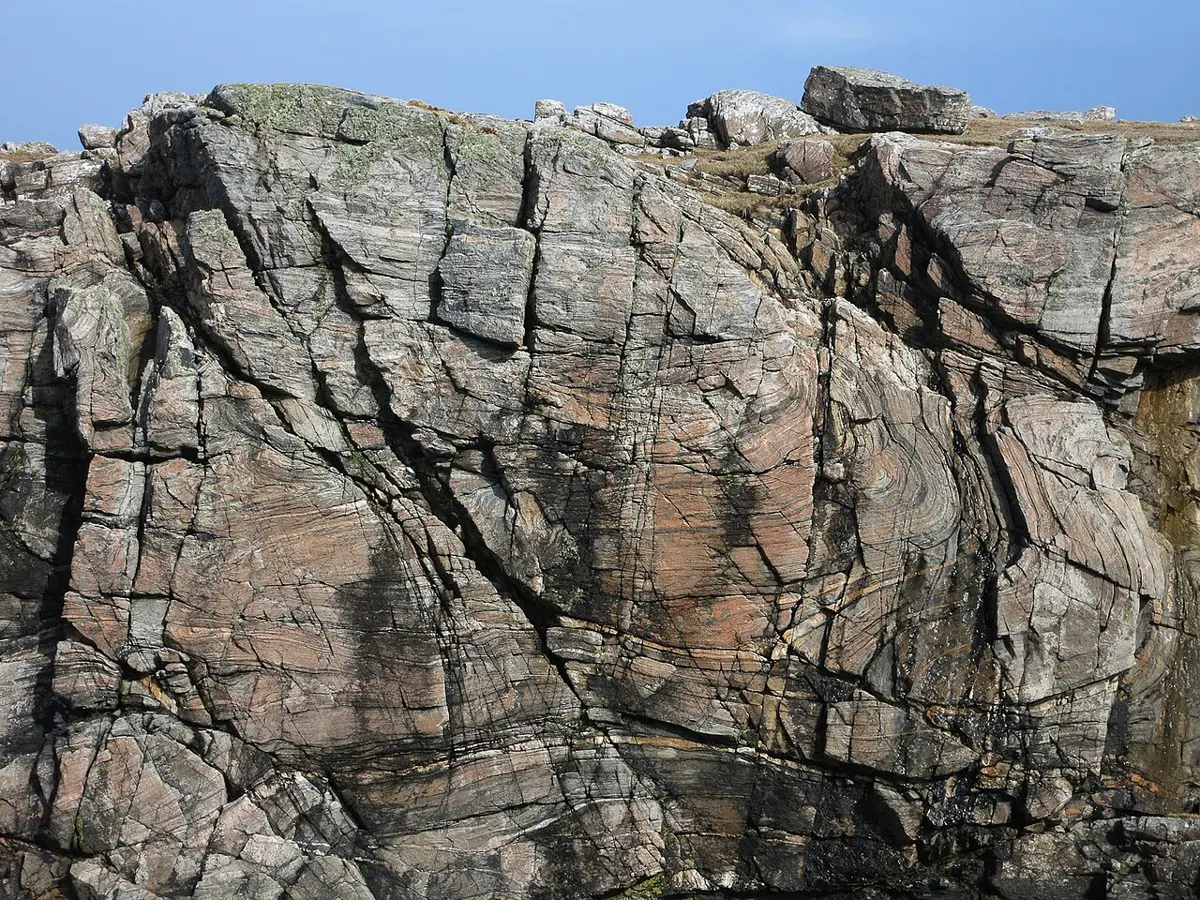 A rock face with wavy, folded bands of light and dark gray