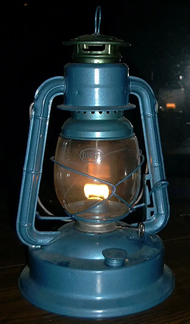 A blue metal kerosene lantern with a glass globe, its flame lit, on a dark table