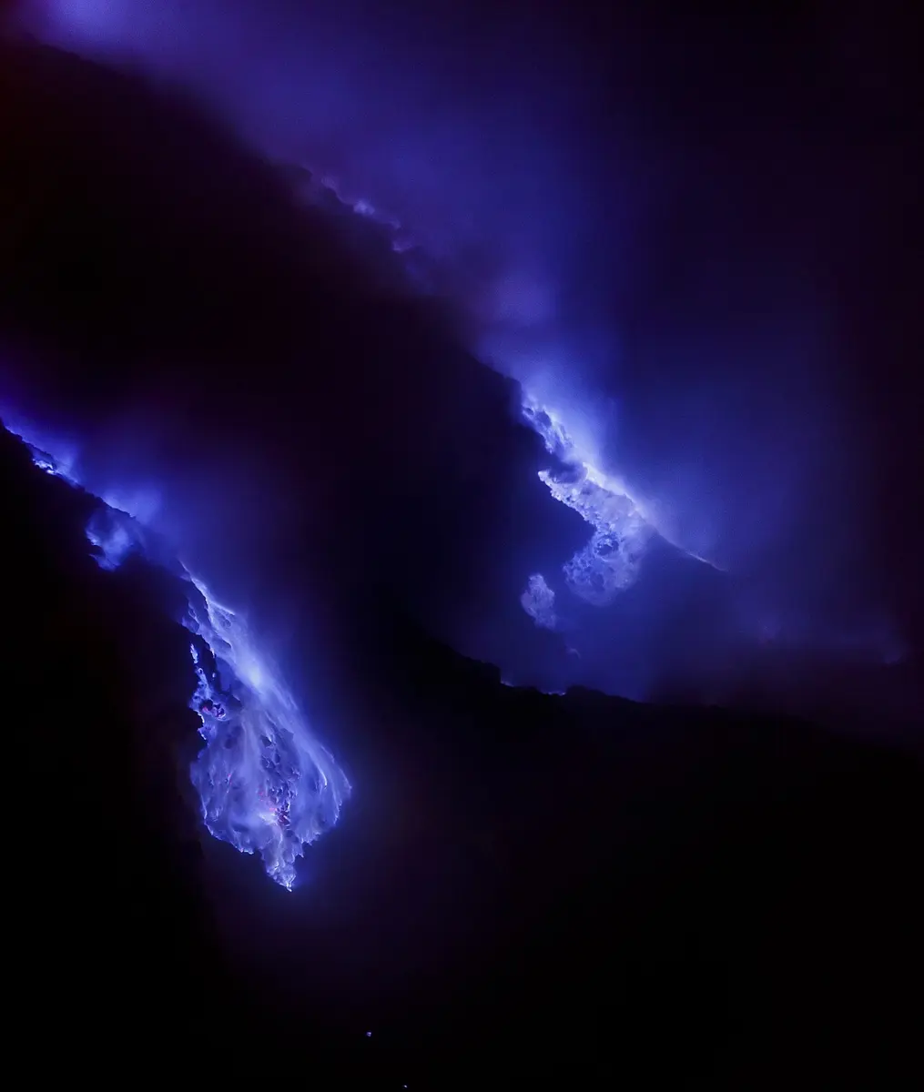 Blue flames rising from rocks in the dark at a volcano