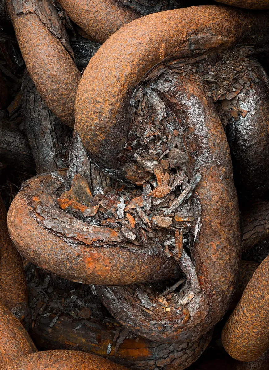 Thick links of an old iron chain covered in orange-brown rust, which is flaking off in layers