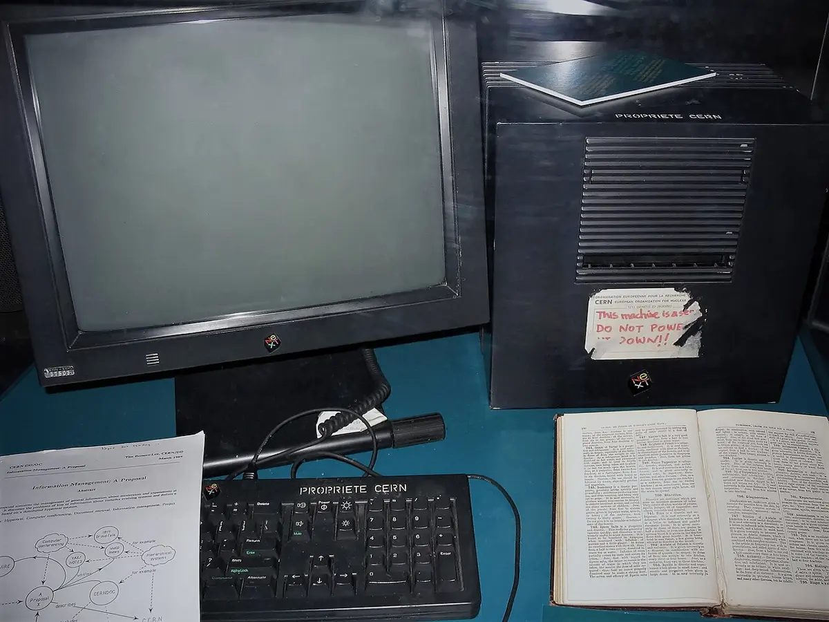 A black NeXT computer in a glass case with a label stuck on it reading: This machine is a server. DO NOT POWER IT DOWN!!