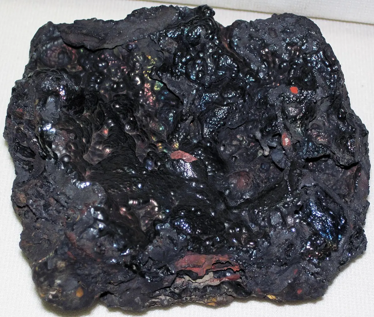 A rough, shiny black lump of mineral with a few reddish patches