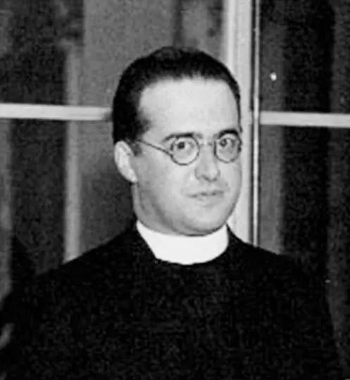 An old black-and-white photograph of a man in round glasses and a priest's collar