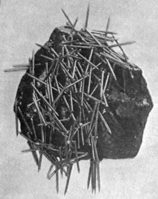 A dark, rough lump of lodestone with small iron nails sticking to it