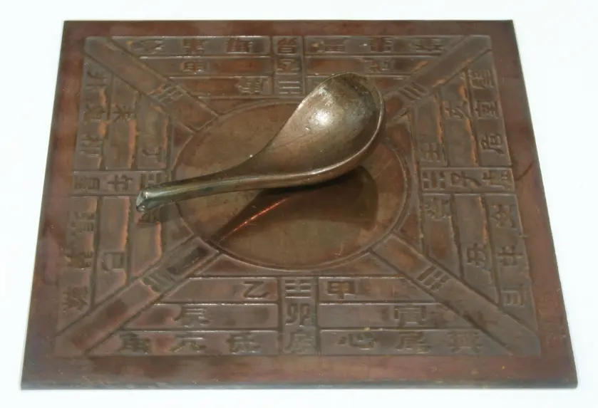 A spoon resting on a square bronze plate carved with Chinese characters for the directions